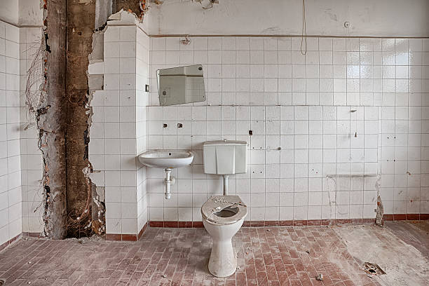 Demolished bathroom with crumbling tile and exposed pipes